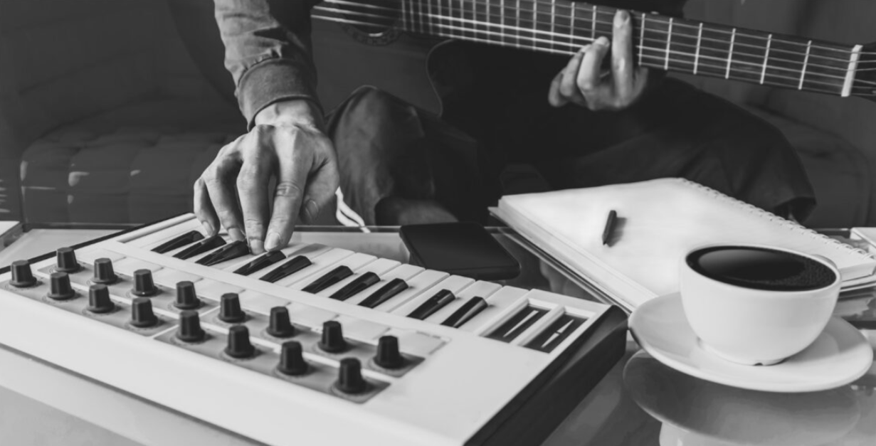 Person playing keyboard with one hand and holding guitar in the other
