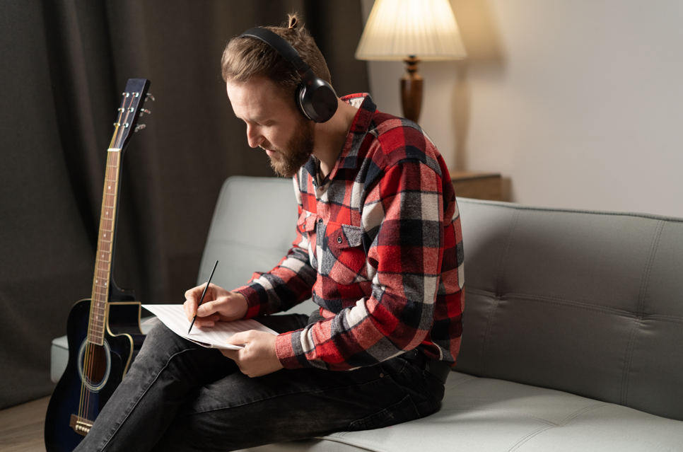 Man writing song with guitar next to him